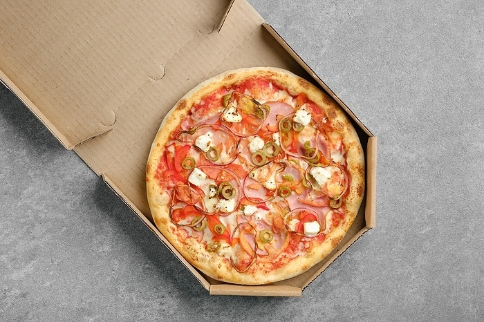 Top view of pizza with ham, onion, olives and feta cheese in cardboard box