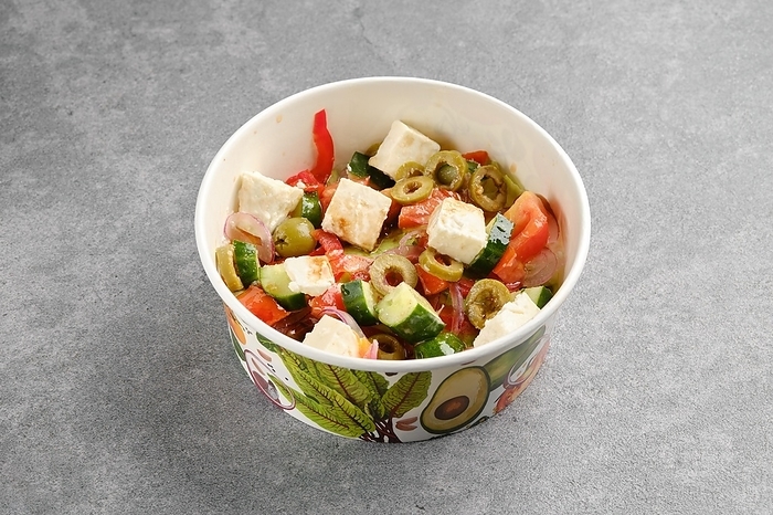 Salad with feta cheese, tomatoes, iceberg lettuce, red onion and olives in cardboard bowl