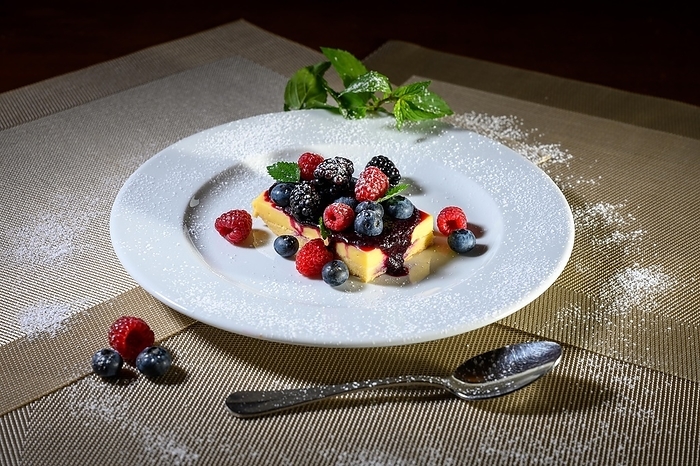 A slice of cheesecake with fresh raspberries and blackberries and a layer of icing sugar on a white plate