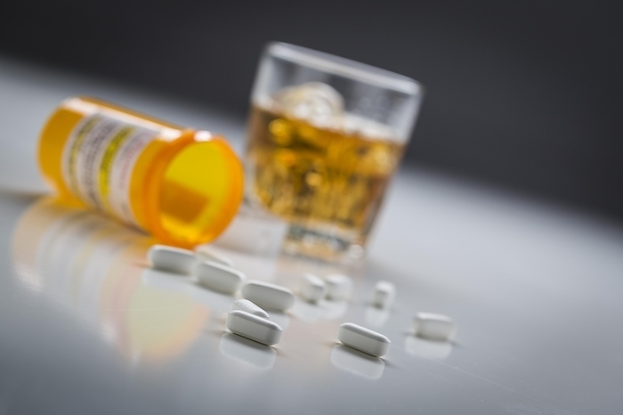 Several prescription drugs spilled from fallen bottle near glass of alcohol