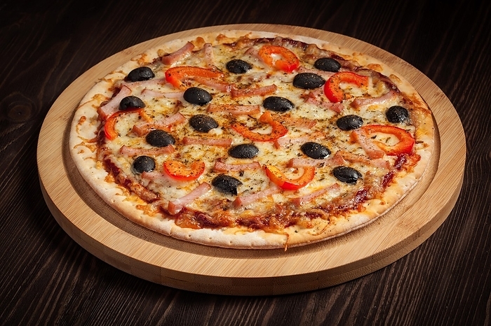 Ham pizza with (capsicum) and olives on wooden board on table