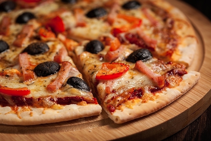 Sliced ham pizza with (capsicum) and olives on wooden board on table