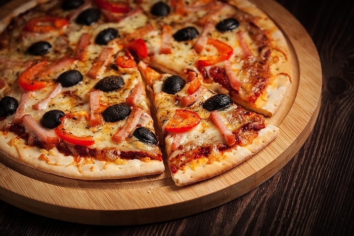 Sliced ham pizza with (capsicum) and olives on wooden board on table