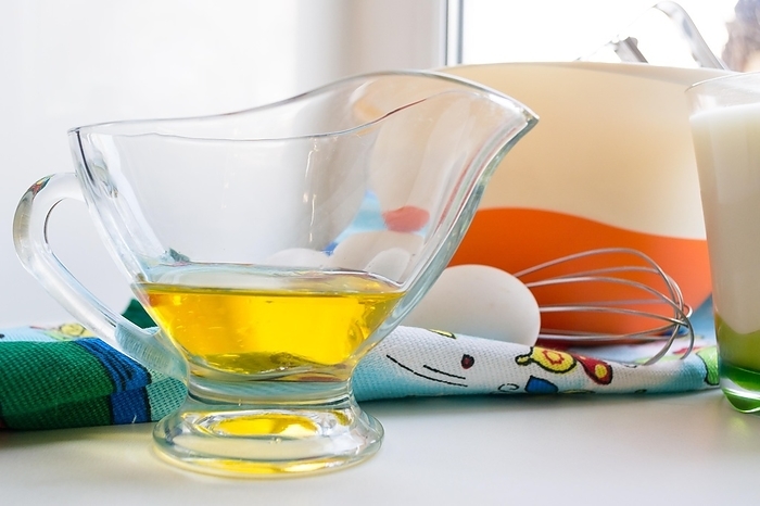 Sunflower oil in a glass transparent oiler on a white windowsill next to the ingredients for pancakes, close up
