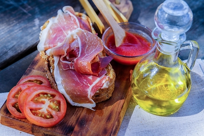 Toast of bread with tomato, olive oil and ham acorn-fed typical spanish toast prepared on a wooden table in the countryside