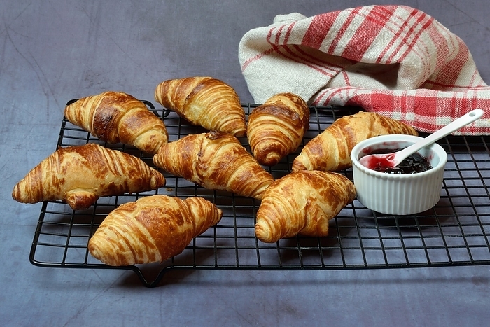 Several croissants on baking rack and bowl with jam, croissants