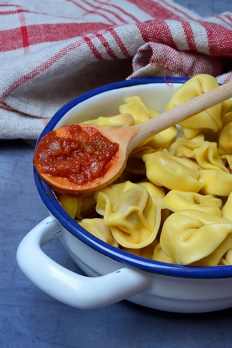 Pasta in pot and cooking spoon with tomato sauce, tortelloni