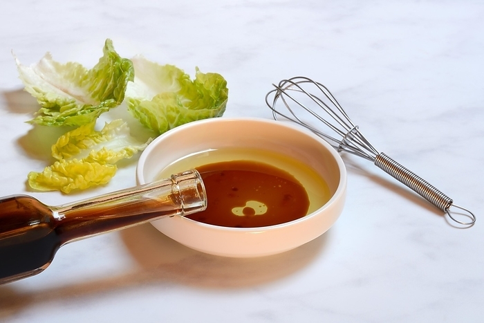 Bowl with cooking oil and aceto balsamico, bottle and whisk, salad leaves