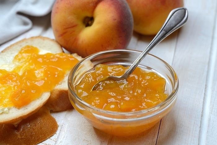 Peach jam in a glass bowl with spoon, slice of bread and peaches
