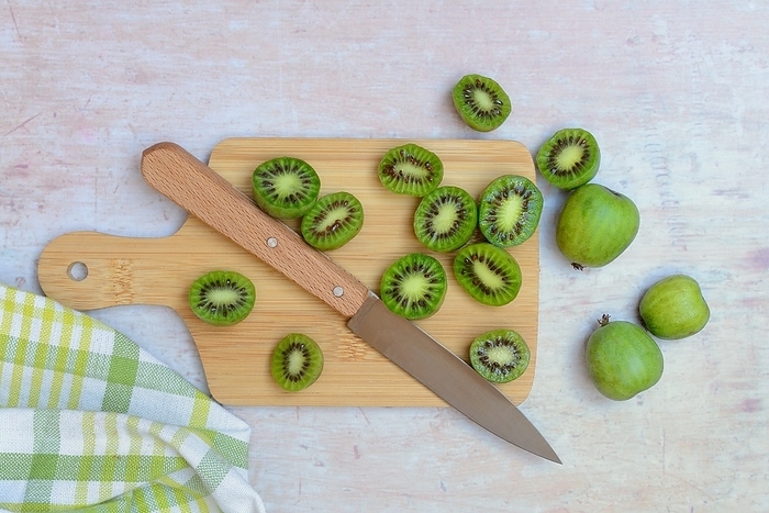 Mini kiwi, whole and halved fruit on wooden board with knife (Actinidia arguta)