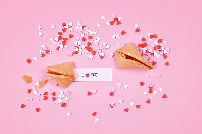 Fortune cookies with text 'I love you' and sugar sprinkle hearts on pink background