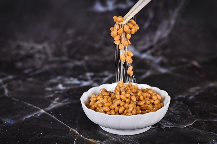 Traditional Japanese food Natto made from fermented soybeans drawing sticky strings on chopsticks on dark background