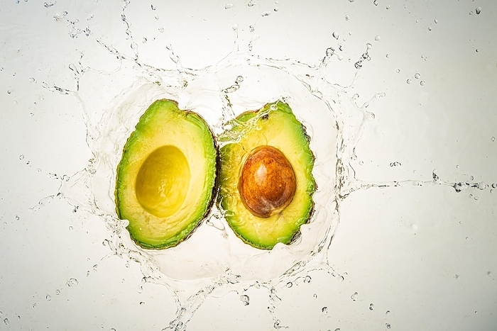 Two halves of avocado splashing into clear water, light background