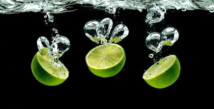 Three lime halves, splashing into water against black