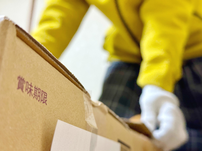 A man with military gloves trying to lift a cardboard box with expiration date lettering.