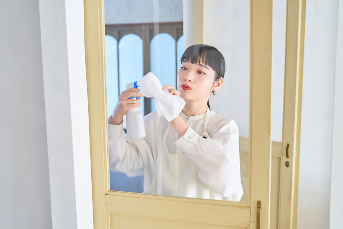 A young Japanese woman cleaning the glass in her room.