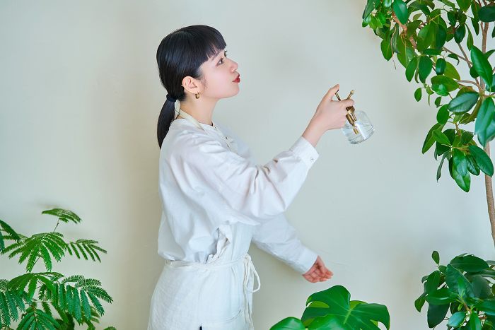 A young Japanese woman watering a houseplant in her room.