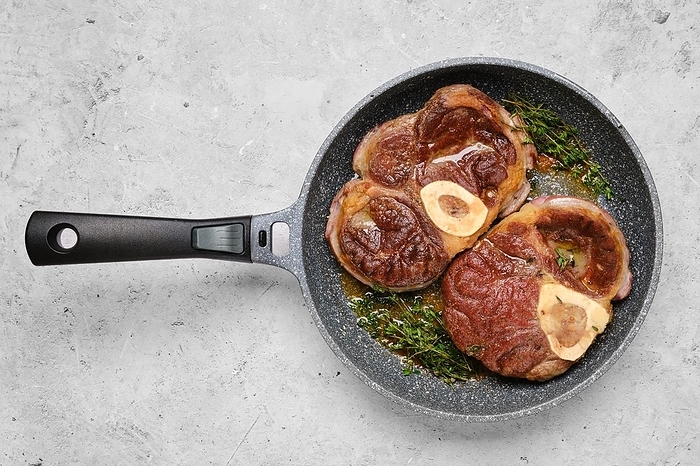 Two pieces of beef meat ossobuco in a frying pan with thyme, by Aleksei Isachenko