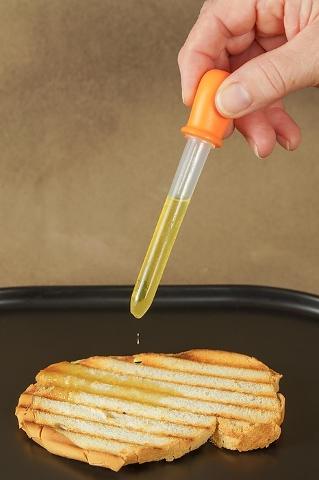 Woman pours olive oil on toast with an dropper because of excessive oil prices, by jose hernandez antona