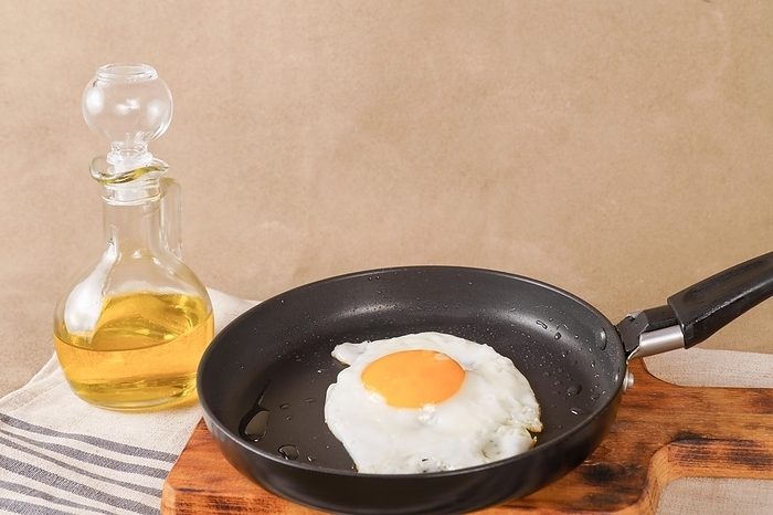 Fried egg with extra virgin olive oil in a frying pan with a glass bottle with oil on a wooden board, by jose hernandez antona