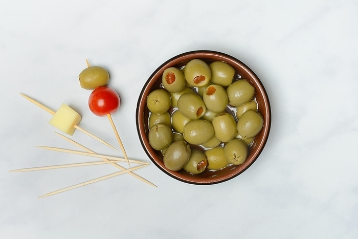 Green olives stuffed with pepper pieces, in bowl, toothpick with olive and cheese cube, by Jürgen Pfeiffer