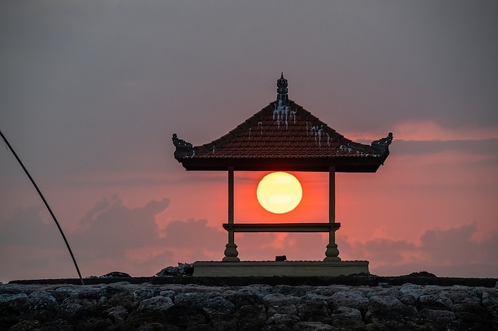 Sunrise on sandy beach with small temples in the water. Landscape shot with red circular sun on the beach of Sanur, Bali, Indonesia, Asia, by Jan Wehnert