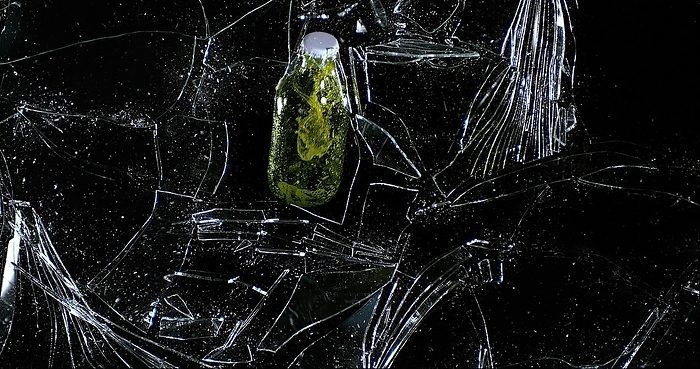 Bottle of Beer breaking Pane of Glass against Black Background, by Lacz Gerard