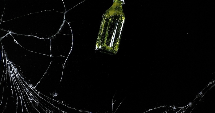 Bottle of Beer breaking Pane of Glass against Black Background, by Lacz Gerard