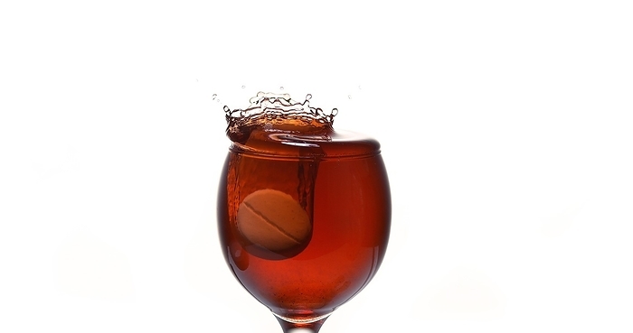 Tablet Falling into a Glass of red Wine against White Background, by Lacz Gerard