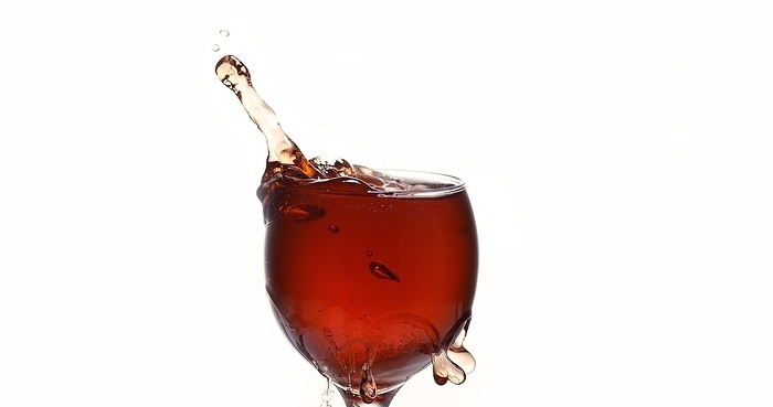 Tablet Falling into a Glass of red Wine against White Background, by Lacz Gerard