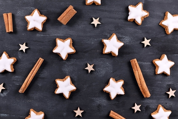 Traditional German star shaped glazed cinnamon Christmas cookies called 'Zimtsterne' on dark black background with star ornaments and cinnamon sticks, by Firn