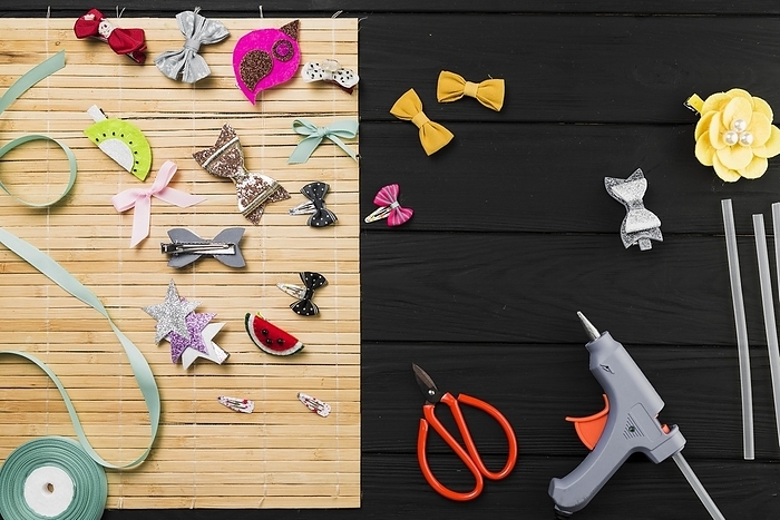 Top view hot glue gun scissor ribbon colorful hair clips place mat against wooden table, by Oleksandr Latkun