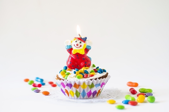 Decorative cup cake with illuminated clown candle white background, by Oleksandr Latkun