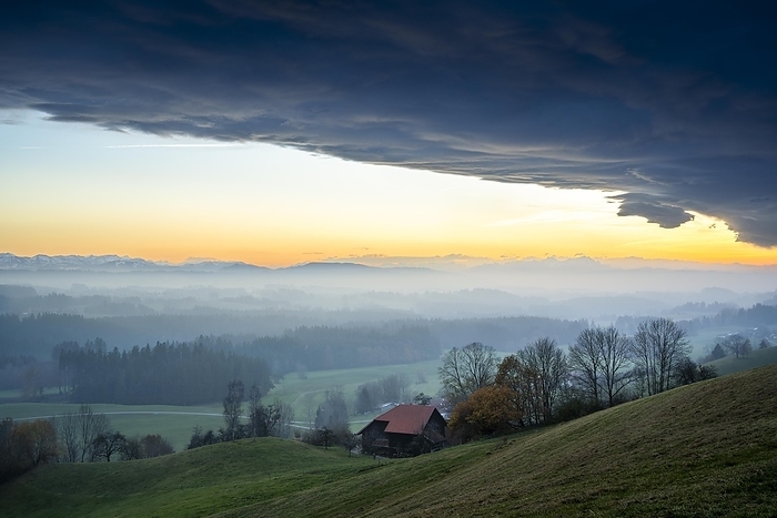 View from the Siggener Höhe on landscape in the Allgäu to the Alps after sunset. A farm in the foreground, others further back. Clouds of fog over the forests, autumn. Dramatic cloud atmosphere in the sky. Siggen, Allgäu, Baden-Württemberg and Bavaria, Germany, Europe, by Susanne Fritzsche