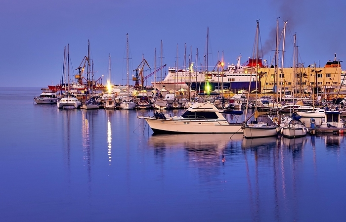 View of port area and bay in Heraklion, capital of Crete island, Greece. Ferries and cruises, fishing boats moored in harbor at sunset. Clear blue sky, deep blue waters, yachts, sailboats. Travel destination of Mediterranean sea, summer vacations, by Natallia Pershaj
