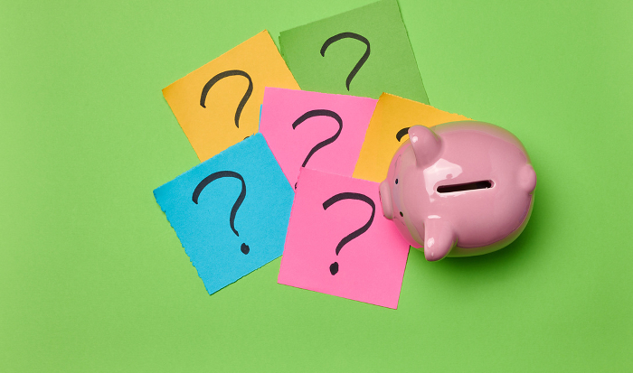 Ceramic piggy bank and stickers with drawn question marks on a green background, top view Ceramic piggy bank and stickers with drawn question marks on a green background, top view