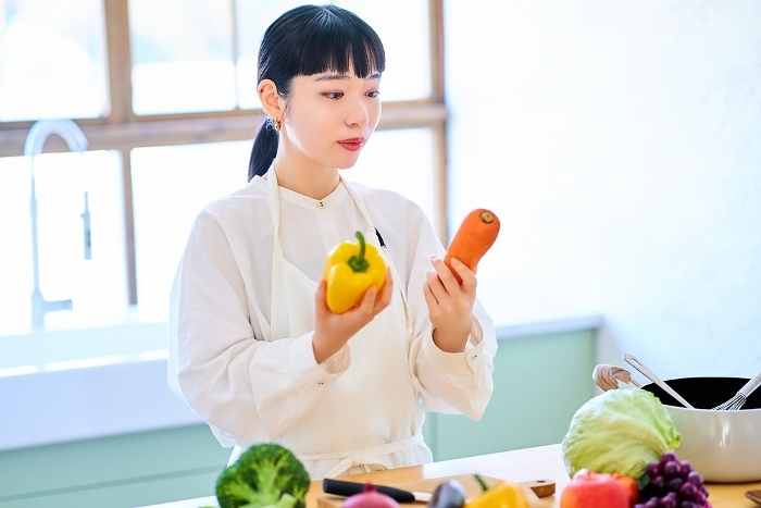 A young Japanese woman holding vegetables in her kitchen (People)