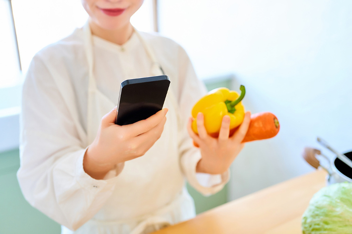 Young woman in kitchen with vegetables and smartphone in hand