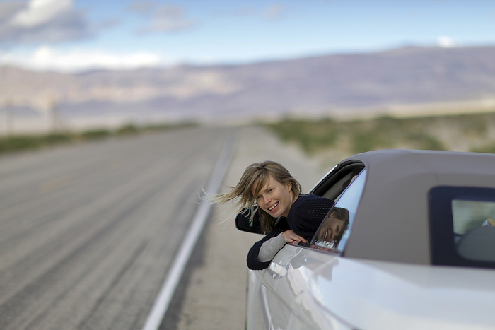 America A Young Woman Leaning Out Of Her Car Window On A Deserted Road In The Desert On Highway 190  California, United States Of America, by Timothy Allen   Design Pics