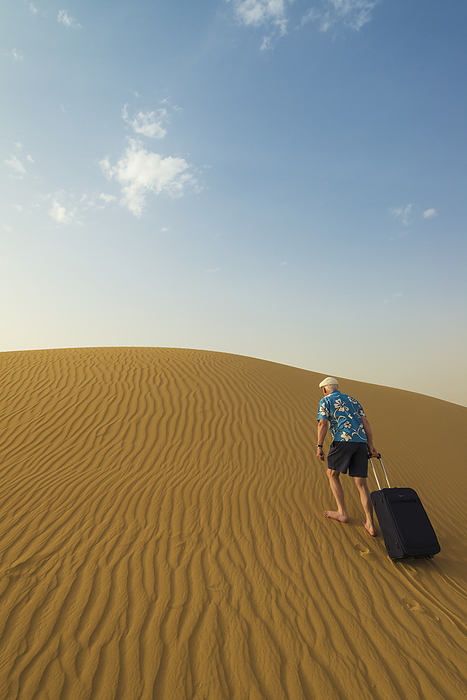 UAE Dubai Barefoot Man With Suitcase Walking Up Sand Dune  Dubai, United Arab Emirates, by Ian Cumming   Design Pics
