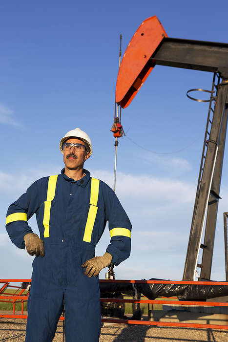 Canada Male Oil Worker With Hard Hat, Eye Protection, Leather Gloves And Protective Coveralls Standing With Pump Jack In The Background With Blue Sky And Clouds  Alberta, Canada, by Michael Interisano   Design Pics