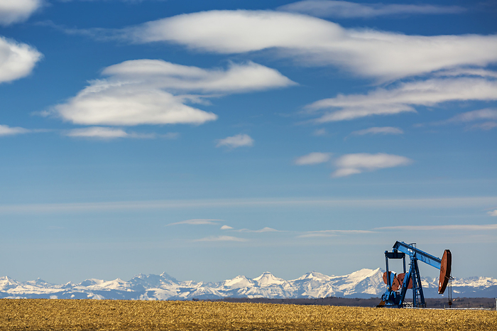 Canada Pump Jack In Stubble Field With Snow Covered Mountains In The Background With Blue Sky And Clouds  Alberta, Canada, by Michael Interisano   Design Pics