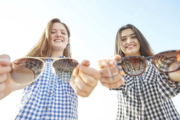 Toronto, Canada Two teenage girls posing and holding out their sunglasses towards the camera as if offering them to the viewer, Woodbine Beach  Toronto, Ontario, Canada, by Vast Photography   Design Pics