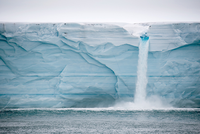 Meltwater pours over an ice cliff from the surface of the Nordaustlandet ice cap; Svalbard, Norway, by Michael Melford / Design Pics