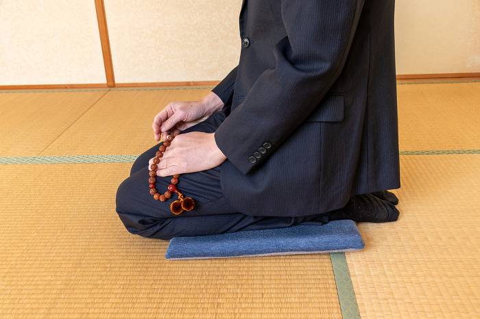 A man sitting on the floor with prayer beads in his hands in a tatami matted Japanese room
