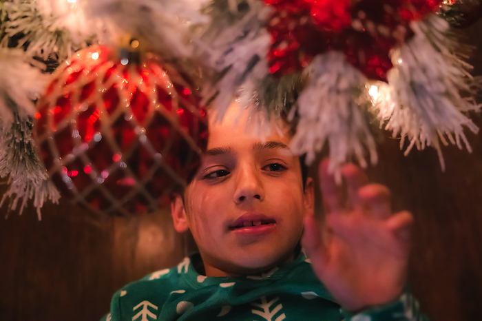 Boy in pajamas looking up through a Christmas tree, by Cavan Images / Christianne Dowd