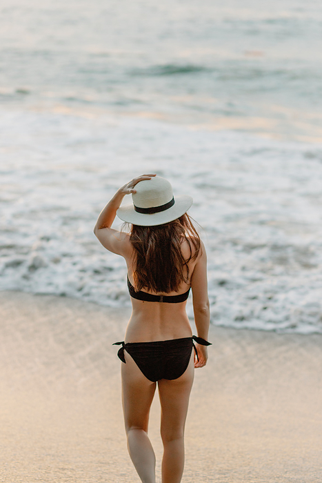 Brunette in black bikini gazes horizon, seaside serenity., by Cavan Images / Samantha Joy Shantz Photography