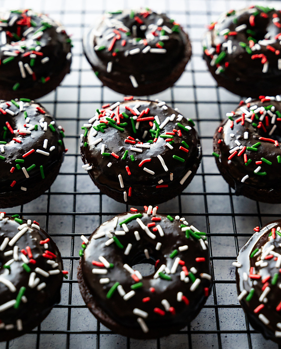 Close up of chocolate glazed donuts with Christmas sprinkles., by Cavan Images / Dorene Hookey