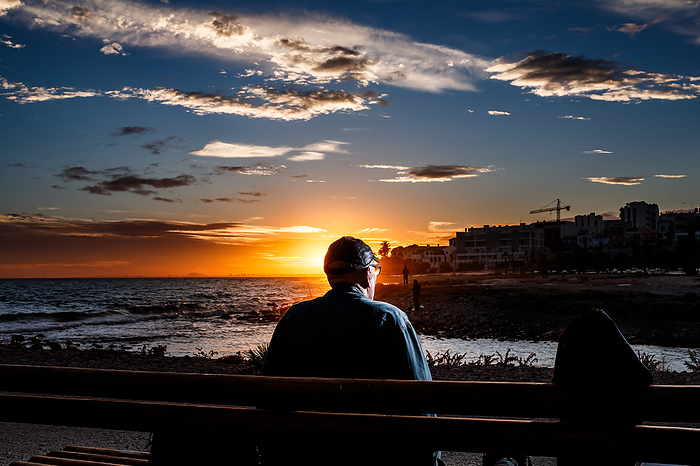 Calm man sitting on a bench watching the sunset, by Cavan Images / Lazareto