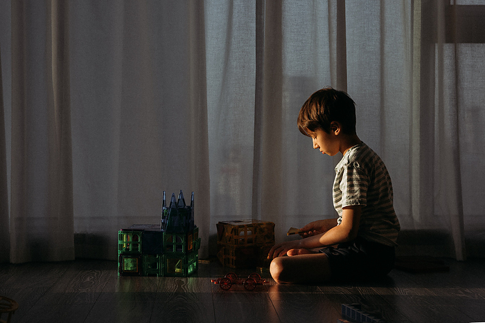 The boy plays the constructor on the floor in the sun, by Cavan Images / Natalia Akulova